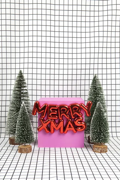 メリーXmasといくつかの小さなクリスマスツリーとグラフィックブラックとホワイトグリッドの背景に黄色のキューブで構成されたミニチュアの森のシーンを言った光沢のある赤いプラスチック製のクリスマスの装飾 最小限の静止した写真 — ストック写真