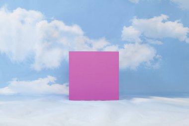 Pembe bir küp, bulutlu mavi gökyüzünün ortasında ahşap bir ekran standı. Asgari natürmort
