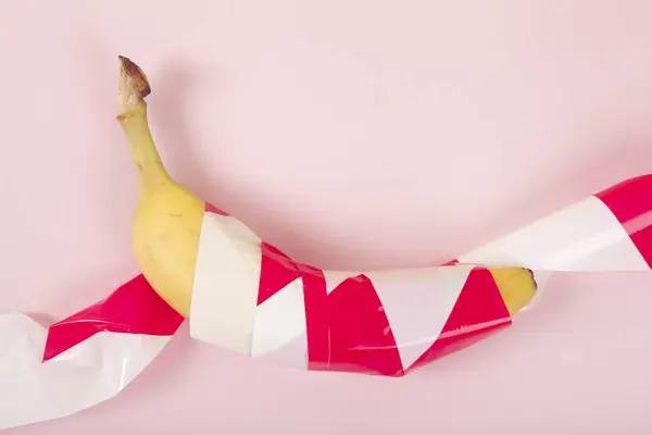 赤と白のプラスチック製のリボンに包まれた熟したバナナが捕獲されました 鮮やかな色と最小限のポップアート写真 ロイヤリティフリーのストック画像