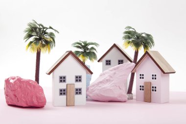 Farklı renklerde boyanmış palmiye ağaçları ve kayalarla çevrili pembe bir tatil köyünü temsil eden minyatür yazlık evlerin maketi. Parlak renkler ve minimal pop sanat fotoğrafçılığı