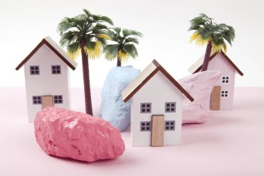 model of miniature beach houses representing a vacation village in a harmony of pink surrounded by palm trees and rocks painted in different colors. Bright colors and minimal pop art photography clipart