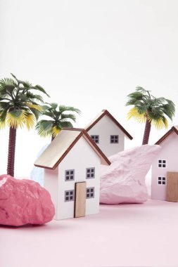 Farklı renklerde boyanmış palmiye ağaçları ve kayalarla çevrili pembe bir tatil köyünü temsil eden minyatür yazlık evlerin maketi. Parlak renkler ve minimal pop sanat fotoğrafçılığı
