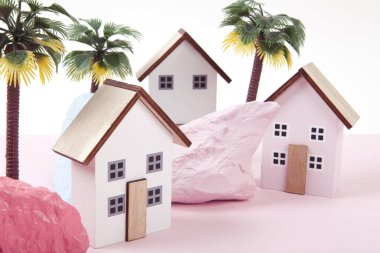 model of miniature beach houses representing a vacation village in a harmony of pink surrounded by palm trees and rocks painted in different colors. Bright colors and minimal pop art photography clipart