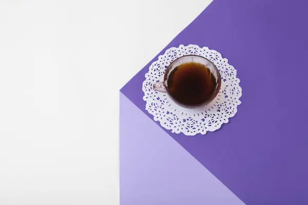 a violet cube made with colored paper to create a 3D optical illusion. On top is a vintage pink coffee cup with a white lace doily. Vivid colors and minimal pop art photography.