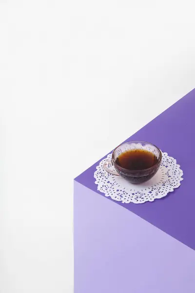3D光学錯覚を作成するために色紙で作られたバイオレットキューブ 上には白いレースが施されたヴィンテージピンクのコーヒーカップがあります 鮮やかな色と最小限のポップアート写真 ストック画像