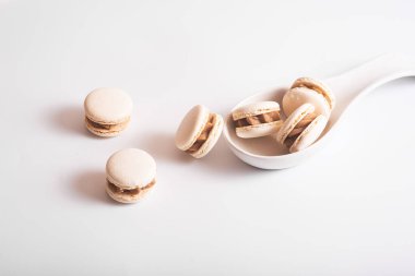 Tasty almond macarons in ceramic white spoon on white background. Copy space. Front view, text place, flat lay