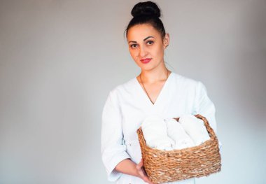 a young woman of European appearance in a white medical uniform with white towels in her hand on the white background. Booking a time for a massage session, Making an appointment. promotion of masage