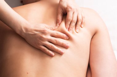 masseur massaging back and shoulder blades of young woman on massage table on white background. Concept of massage spa treatments. Close-up
