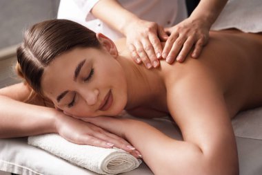 masseur massaging back and shoulder blades of young woman smiling on massage table on white background. Concept of massage spa treatments. Close-up