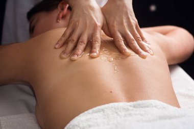 young woman lying on the table and getting spa procedure massage with honeyed in dark room. Masseuse pours honey on client's back. relaxing and beneficial spa treatments for the skin