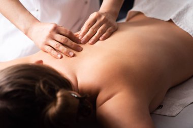 Masör, masaj masasında beyaz arka planda genç bir bayanın sırt ve omuz bıçaklarına masaj yapıyor. Masaj spa tedavisi kavramı. Vücut gevşeme prosedürleri. Yakın plan.