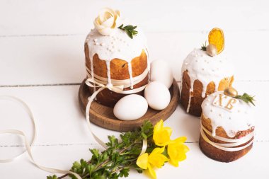 Hassas, hafif, modern tasarımı olan paskalya pastaları ve sarı nergisli beyaz ahşap arka planda yumurtalar. Paskalya konsepti. Geleneksel Paskalya yemekleri. Paskalya sembolü