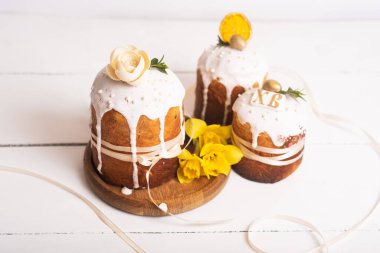 Hassas, hafif, modern tasarımı olan paskalya pastaları ve sarı nergisli beyaz ahşap arka planda yumurtalar. Paskalya konsepti. Geleneksel Paskalya yemekleri. Paskalya sembolü