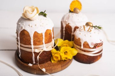 Hassas, hafif, modern tasarımı olan paskalya pastaları ve sarı nergisli beyaz ahşap arka planda yumurtalar. Paskalya konsepti. Geleneksel Paskalya yemekleri. Paskalya sembolü