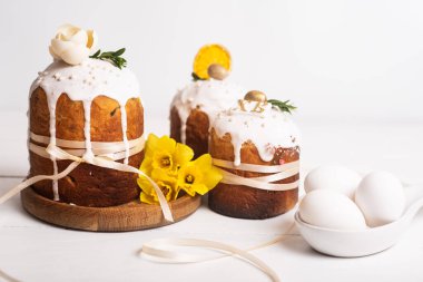 Hassas, hafif, modern tasarımı olan paskalya pastaları ve sarı nergisli beyaz ahşap arka planda yumurtalar. Paskalya konsepti. Geleneksel Paskalya yemekleri. Paskalya sembolü