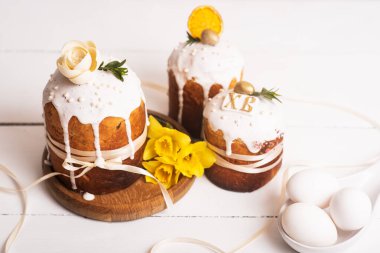 Hassas, hafif, modern tasarımı olan paskalya pastaları ve sarı nergisli beyaz ahşap arka planda yumurtalar. Paskalya konsepti. Geleneksel Paskalya yemekleri. Paskalya sembolü