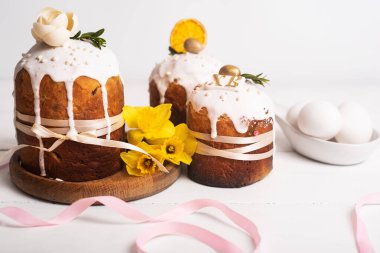 Hassas, hafif, modern tasarımı olan paskalya pastaları ve sarı nergisli beyaz ahşap arka planda yumurtalar. Paskalya konsepti. Geleneksel Paskalya yemekleri. Paskalya sembolü