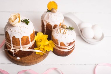 Hassas, hafif, modern tasarımı olan paskalya pastaları ve sarı nergisli beyaz ahşap arka planda yumurtalar. Paskalya konsepti. Geleneksel Paskalya yemekleri. Paskalya sembolü