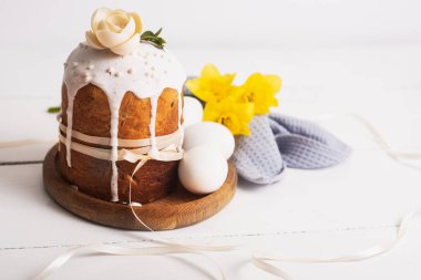 Easter cakes with a delicate, light, modern design nd eggs on a white wooden background with yellow daffodils. Easter concept. Easter traditional food. Easter symbol clipart