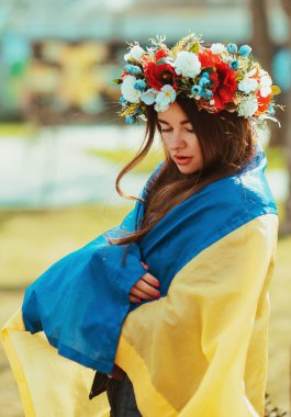 Üzgün, genç bir kadın Ukrayna bayrağına sarılmış kafasında çiçeklerle. Vatanseverlik kavramı. Ukraynalı. Gönüllü olmak, bağış yapmak, minnettarlık sembolü.