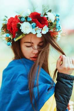 Üzgün, genç bir kadın Ukrayna bayrağına sarılmış kafasında çiçeklerle. Vatanseverlik kavramı. Ukraynalı. Gönüllü olmak, bağış yapmak, minnettarlık sembolü.
