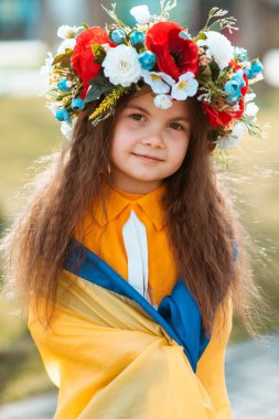 Küçük şirin kız Ukrayna bayrağına sarılmış kafasında çiçek çelengiyle. Vatanseverlik kavramı. Ukrayna Vatanseverliği kavramı. Ukraynalı. Gönüllü olmak, bağış yapmak, minnettarlık sembolü.