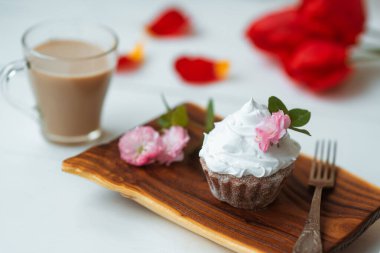 Kek ve kahve. Kremalı lezzetli pasta ve ahşap tabakta pembe çiçek dekoru. Arka planda kırmızı çiçekler. İyi sabahlar. Mükemmel kahvaltı.