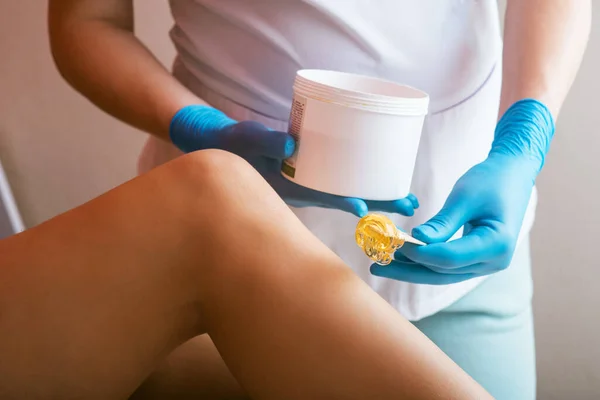 stock image Hands of a cosmetologist close-up, in blue gloves, applying sugar paste on a womans leg. Depilation procedure with sugar paste. hair removal. Details of epilation process. Professional cosmetologist