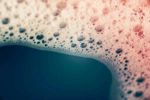 Su yüzeyinde köpüren kalın sabun köpükleri. Güzel parlak, modaya uygun renkler, maviden kırmızıya değişim. Makro. Sabun köpüğü dokusu, köpük.