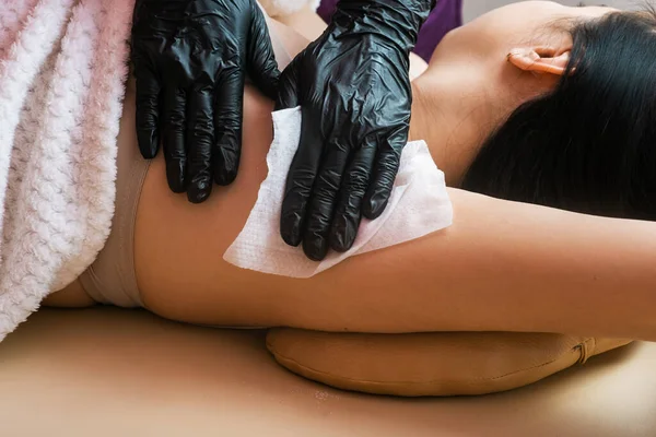 A master cosmetologist in black gloves treats the armpit area after the depilation procedure with sugar paste. hair removal. Details of epilation process
