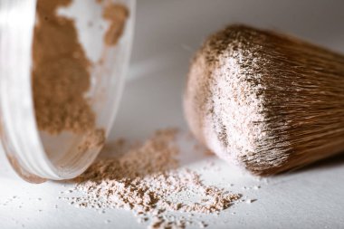 Parçalanmış makyaj tozu çıplak bir tonda ve beyaz arka planda büyük bir toz fırçası ile. Macro, yakın plan. Boşluğu kopyala, metin için yer, Kozmetik kavramı