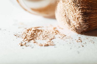 Parçalanmış makyaj tozu çıplak bir tonda ve beyaz arka planda büyük bir toz fırçası ile. Macro, yakın plan. Boşluğu kopyala, metin için yer, Kozmetik kavramı
