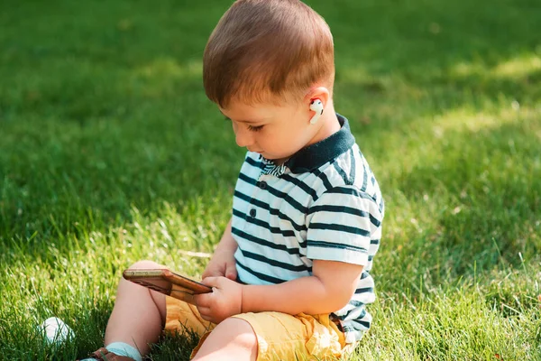 유럽의 귀여운 잔디에 헤드폰을 스마트폰을 사용하고 어린아이는 기계를 어린이의 — 스톡 사진