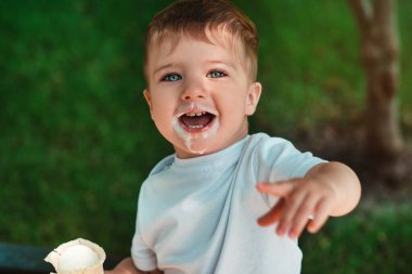 Vanilyalı dondurma yiyen tatlı küçük bir çocuk. Yüzüne dondurma bulaşmış. Komik küçük adam. Bir çocuğun duygusal yakın plan portresi. Yaz zamanı, sütlü tatlı, mutlu bir çocukluk. Çocuklar.