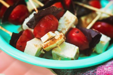 Piknik kanapeleri. Tahta çubuklarda kiraz domatesleri, peynir ve fesleğen yaprakları. Tabakta aperatifler. Lezzetli ve sağlıklı atıştırmalıklar, makro.