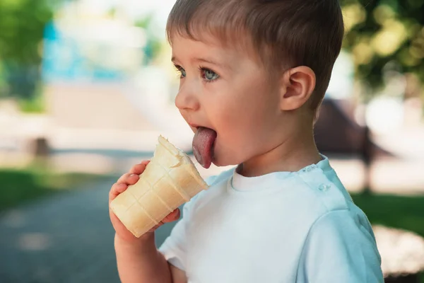 stock image A cute little European-looking baby boy is eating an ice cream cone in a waffle cup outdoors. Close-up. Summertime, milk dessert, happy childhood. Emotions happiness. Childrens joy