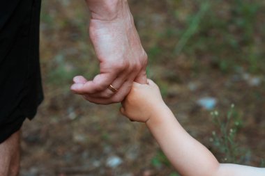 Babası küçük oğlunun elini tutuyor. Yakın plan. Bir babanın sevgisi ve bakımı. Babasıyla ormanda bir yürüyüş. Babalar Günü. Babalık. Film tarzında güzel sanatsal fotoğraf işleme