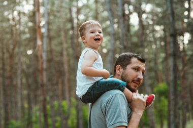 Babalar Günü. Mutlu Avrupalı görünümlü baba ormanda omuzlarında iki yaşındaki oğluyla yürür. Babalık, mutlu bir çocukluk. Mutlu yaz zamanları. Aile kavramı