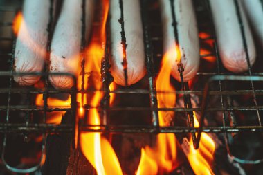 Barbekü ızgarasında süt sosisleri ateşte kızartılır. Ateşin alevlerinde sosisler kapımızda. Lezzetli ızgara sosis. Yaz tatili. Barbekü