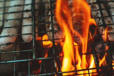 Barbekü ızgarasında süt sosisleri ateşte kızartılır. Ateşin alevlerinde sosisler kapımızda. Lezzetli ızgara sosis. Yaz tatili. Barbekü