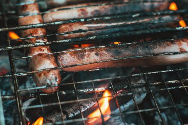 Barbekü ızgarasında süt sosisleri ateşte kızartılır. Ateşin alevlerinde sosisler kapımızda. Lezzetli ızgara sosis. Yaz tatili. Barbekü