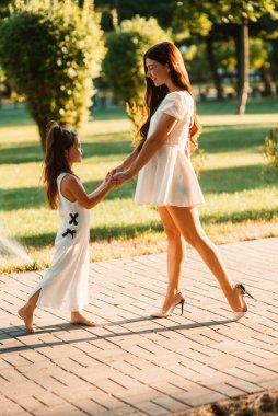 Güzel bir anne dışarıda tatlı küçük kızıyla el ele tutuşur. Mutlu annelikler. Güzel anne ve çocuğu parkta birlikte oynuyorlar. Mutlu bir ailenin portresi. Anneler Günün kutlu olsun.