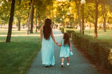 Güzel genç anne parkta genç kızıyla el ele yürüyor. Dikiz aynası. Anne ve kızı dar bir sokakta el ele tutuşarak yürüyorlar. Mutlu Annelik