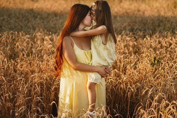 Beautiful young mom and her young daughter cuddling and lounging in a field of wheat at sunset.