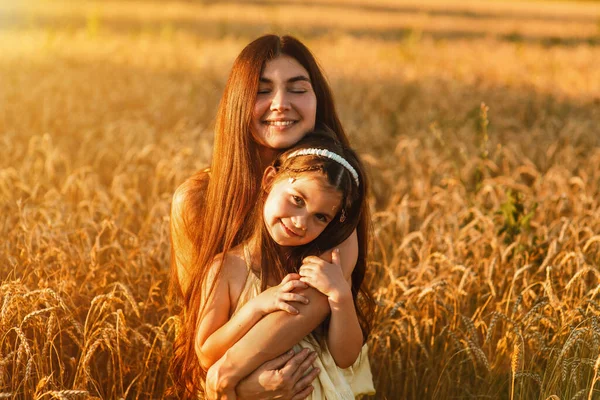Beautiful young mom and her young daughter cuddling and lounging in a field of wheat at sunset.