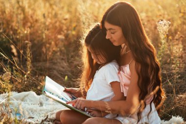 Genç ve güzel bir anne gün batımında çiçeklerle dolu bir tarlanın ortasında beyaz bir yatak örtüsünde genç kızına ilginç bir kitap okuyor. Anne ve kızı dışarıda mutlu vakit geçiriyorlar.