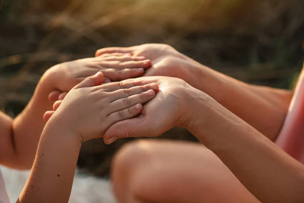 Close up view of young foster parent holding hands of little kid girl, giving psychological help, supporting outdoors at sunset. the concept of a trusting relationship between parent and child