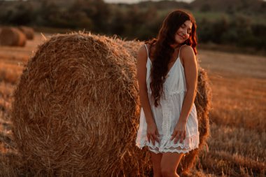 Beyaz saafanlı genç bir kadın gün batımında balyaların arasında buğday tarlasında vakit geçiriyor. Kırsal atmosfer, çiftlikte zaman. Yüksek kalite fotoğraf