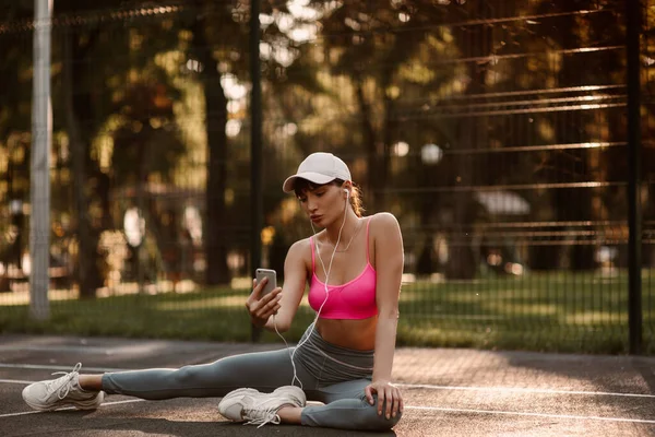Young, beautiful girl listening to music on headphones after a sports practice at the sports ground at sunset. High quality photo
