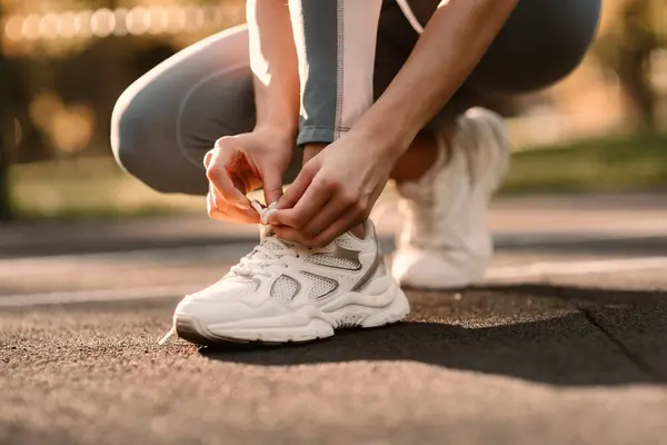 An athlete ties a white sneaker in a close-up on a sports field. Fintes in the open air